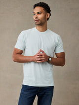 Man wearing light mint green/blue short-sleeve crewneck t-shirt and dark blue jeans, standing 