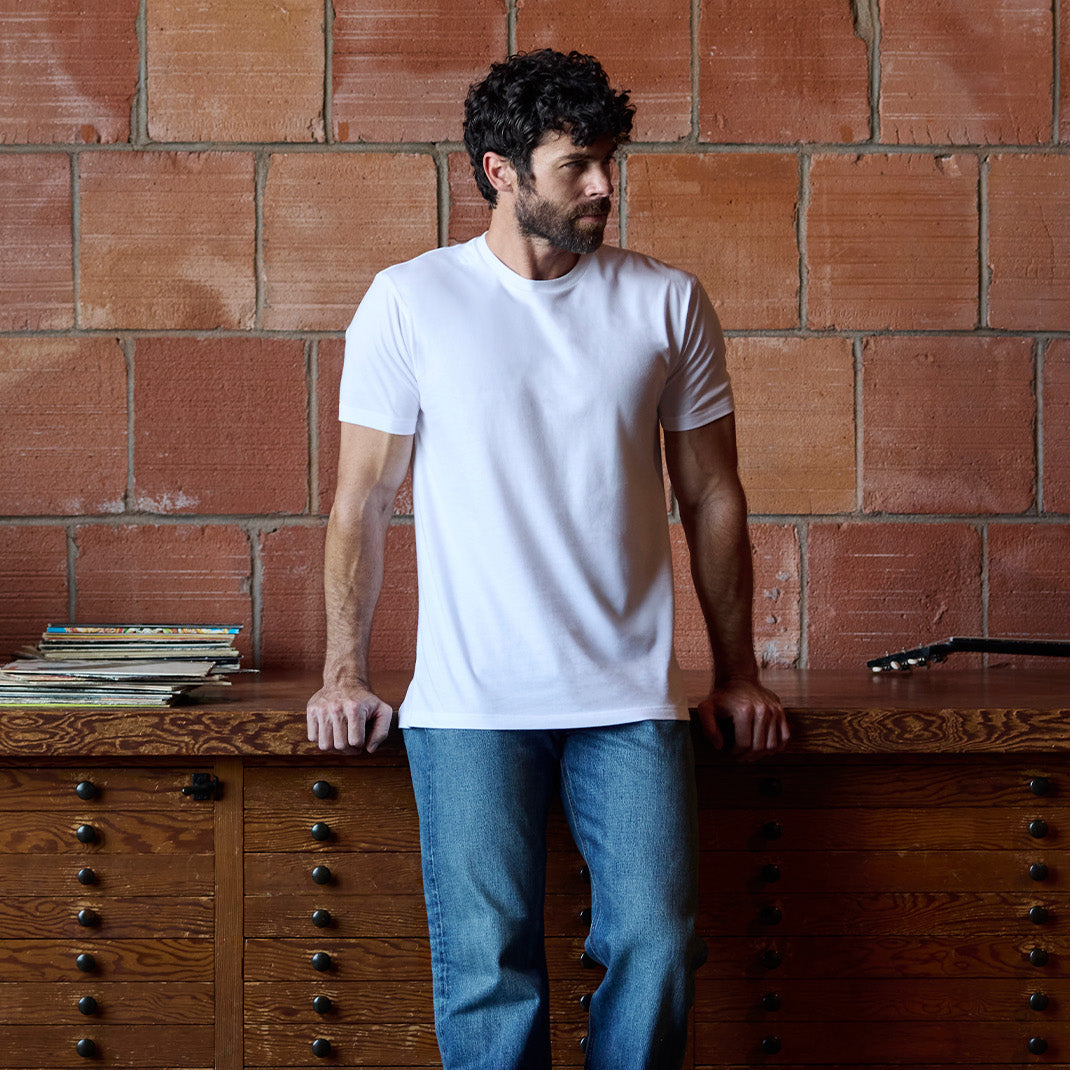 Man wearing Fresh Clean Threads white crew neck tee leaning against dresser